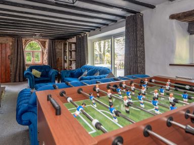 A game room with a foosball table and blue upholstered sofas with exposed ceiling beams and stone walls at Cae Lleci Llanfachreth near Dolgellau