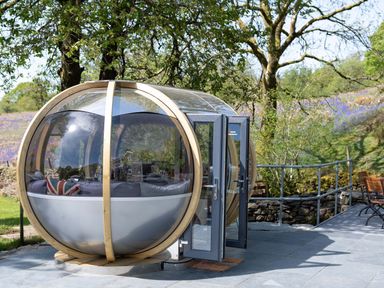 A spherical outdoor pod with glass and wooden frame with grey doors on a stone patio at Cae Lleci in Llanfachreth near Dolgellau