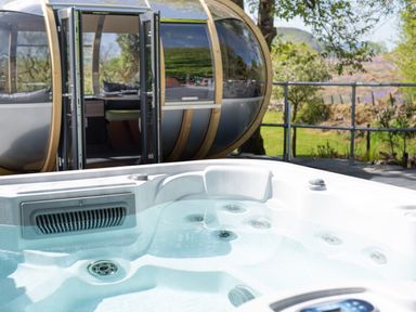 An outdoor hot tub with water in front of a pod accommodation with open doors at Cae Lleci in Llanfachreth near Dolgellau