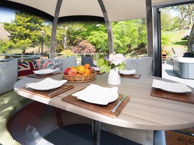 An outdoor dining table set with plates knives and napkins a basket of fruit and a vase with flowers surrounded by cushions at Cae Lleci in Llanfachreth near Dolgellau