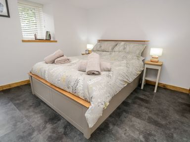 A bedroom with a bed with towels on it bedside tables with lamps and a window with blinds at La'al Riddings Lowick Green Riddings Farm Near Ulverston