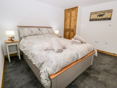 A bedroom with a double bed a wooden door bedside tables with lamps and towels on the bed at La'al Riddings Lowick Green Riddings Farm Near Ulverston