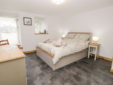 A bedroom with bed side tables lamps a chest of drawers and windows with blinds at La'al Riddings Lowick Green Riddings Farm Near Ulverston