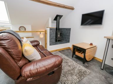 A living room with a brown leather recliner sofa a wall-mounted television and a wood-burning stove at La'al Riddings Lowick Green Riddings Farm Near Ulverston