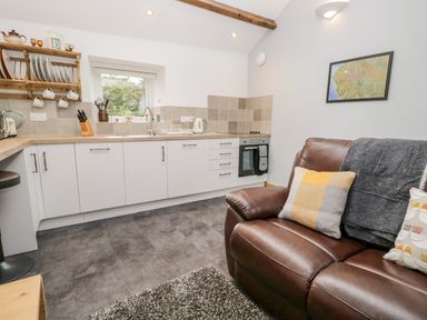 A kitchen with white cabinets a brown leather sofa with pillows and a wall map at La'al Riddings Lowick Green Riddings Farm Near Ulverston