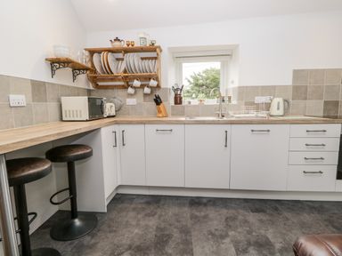 A kitchen with white cabinets wooden shelves and stools at La'al Riddings in Lowick Green Riddings Farm Near Ulverston