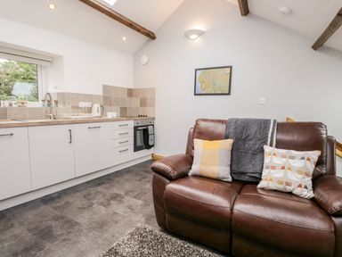 A kitchen area with white cabinets and a brown leather sofa with cushions at La'al Riddings in Lowick Green Riddings Farm Near Ulverston
