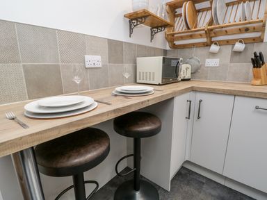 A kitchen corner with two stools plates glasses and cutlery on the counter a microwave knife block and dish rack on the wall at La'al Riddings Lowick Green Riddings Farm Near Ulverston