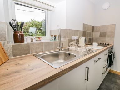 A kitchen countertop with a sink a dish rack a kettle cooking utensils and a window at La'al Riddings in Lowick Green Riddings Farm Near Ulverston