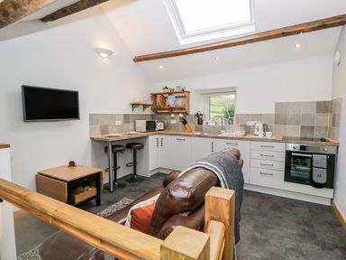 A kitchen with white cabinets wooden countertop bar stools and a brown leather sofa at La'al Riddings in Lowick Green Riddings Farm Near Ulverston