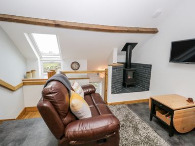A living space with a brown leather sofa pillows a wood stove a wall clock a small wooden table and a skylight window at La'al Riddings in Lowick Green Riddings Farm Near Ulverston