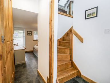 A hallway with wooden stairs and a glimpse of a room with a bed and windows at La'al Riddings Lowick Green Riddings Farm Near Ulverston