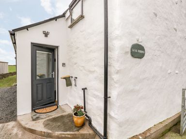 An exterior entrance with a dark door a doormat a flower pot and a sign reading LA'AL RIDDINGS at La'al Riddings Lowick Green Riddings Farm Near Ulverston