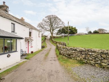 A rural dirt road with stone walls and a white cottage on the left at La'al Riddings Lowick Green Riddings Farm Near Ulverston