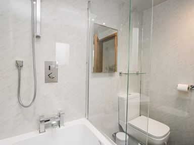 A bathroom with a bathtub shower combination a toilet and a glass divider at La'al Riddings in Lowick Green Riddings Farm Near Ulverston