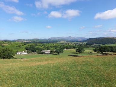 A rural landscape with green fields trees stone walls farm buildings and distant hills at La'al Riddings Lowick Green Riddings Farm Near Ulverston