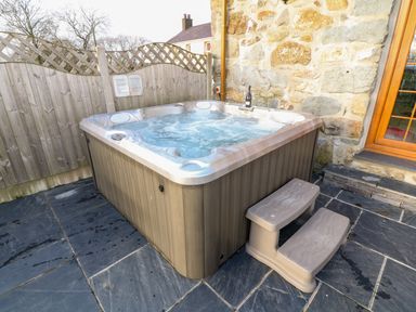An outdoor hot tub with water jets on a tiled patio next to a stone wall and wooden fence at Stabl in Pwllheli