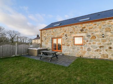 A stone house with skylights a patio table and a hot tub in a fenced garden at Stabl in Pwllheli