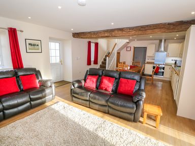 A living room with black leather sofas and red cushions next to an open kitchen with wooden dining table at Stabl in Pwllheli