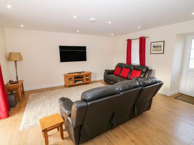 A living room with two black sofas red cushions red curtains a wooden tv stand and a wall mounted tv at Stabl in Pwllheli