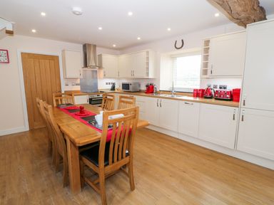 A kitchen with white cabinets and wooden dining table with chairs at Stabl in Pwllheli