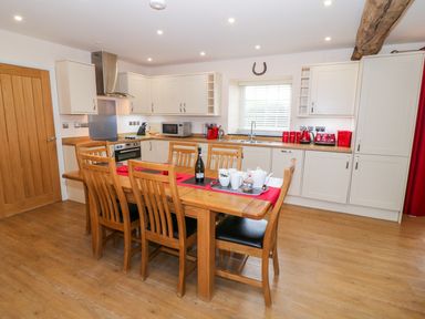 A kitchen with wooden dining table and chairs and white cabinets at Stabl in Pwllheli
