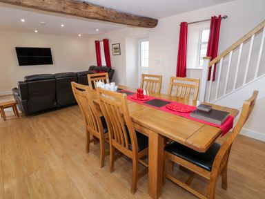 A dining area with wooden table and chairs next to a living room with black leather sofas and a wall-mounted television at Stabl in Pwllheli