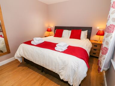 A bedroom with a bed with white and red bedding two wooden bedside tables with lamps and a large mirror on the wall at Stabl in Pwllheli