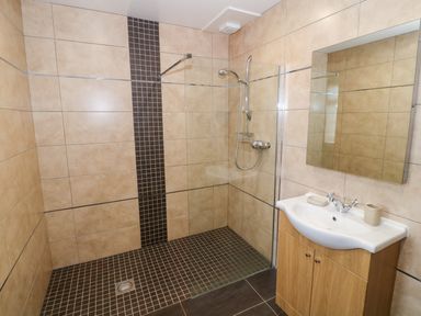 A bathroom with a walk-in shower and a sink with a mirror above at Stabl in Pwllheli