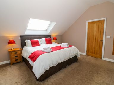 A bedroom with a bed with white and red bedding a wooden door and two bedside tables with lamps at Stabl in Pwllheli