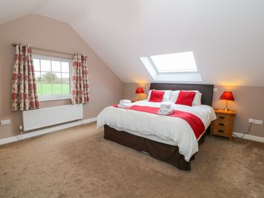 A bedroom with a double bed red cushions lamps and a window at Stabl in Pwllheli