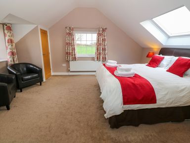 A bedroom with a double bed with red pillows and runners two black armchairs floral curtains and a skylight window at Stabl Pwllheli