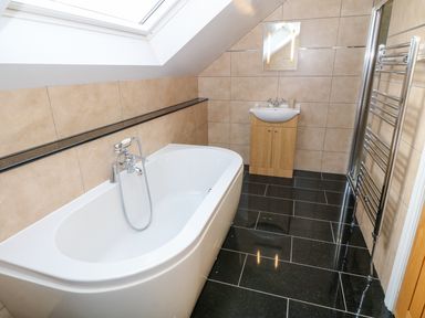 A bathroom with a freestanding bathtub a sink with a cabinet a wall mirror and a heated towel rail at Stabl in Pwllheli