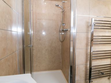A shower area with glass doors a handheld showerhead and a chrome towel rail in a tiled bathroom at Stabl in Pwllheli