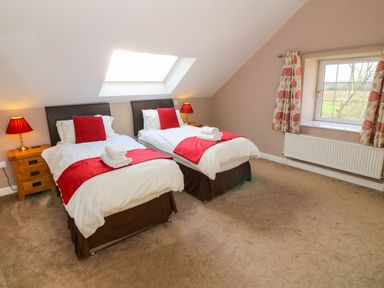 A bedroom with two single beds with red accents and bedside tables under a skylight window at Stabl in Pwllheli