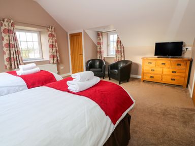 A bedroom with two single beds two black armchairs a wooden dresser with a television and floral curtains at Stabl in Pwllheli