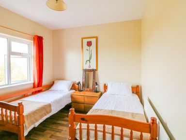 A bedroom with two single beds a wooden nightstand between them and a window with red curtains at The Trawler in Blackwater County Wexford