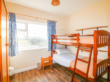 A bedroom with wooden bunk beds a small stool and a wardrobe near a window with blue curtains at The Trawler in Blackwater County Wexford