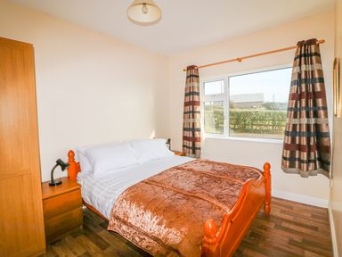 A bedroom with a wooden bed covered with a brown blanket two wooden bedside tables with lamps and a window with striped curtains at The Trawler in Blackwater County Wexford