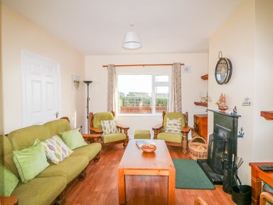 A living room with green armchairs sofa wooden coffee table and fireplace at The Trawler in Blackwater County Wexford