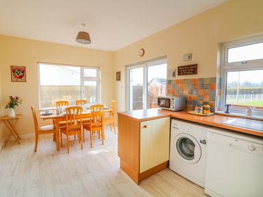 A kitchen and dining area with wooden chairs around a table and appliances by the counter at The Trawler in Blackwater County Wexford