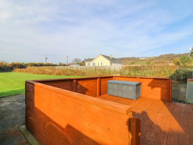 An outdoor wooden deck with storage box surrounded by grass and bushes with a house in the background at The Trawler in Blackwater County Wexford