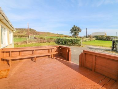 A wooden deck with built in bench seating outside a house overlooking a grassy area and rural landscape at The Trawler in Blackwater County Wexford