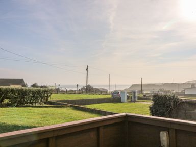 A grassy yard with hedges and a parked car near a gate with a view of the ocean at The Trawler in Blackwater County Wexford
