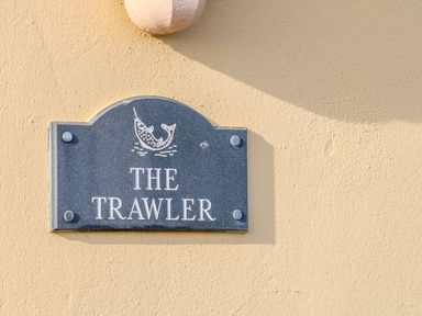 A dark sign with a fish illustration and the text The Trawler on a beige wall at The Trawler in Blackwater County Wexford