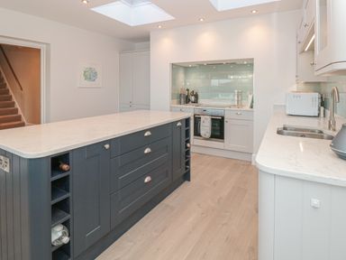 A kitchen with a large island with wine storage white countertops a stove and oven a sink and a microwave at Moorings in Kingswear Devon