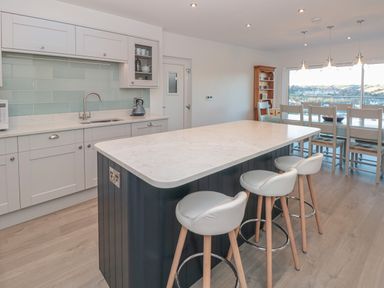 A kitchen with a marble island and three stools next to a dining area with a wooden hutch and large window at Moorings Kingswear Devon