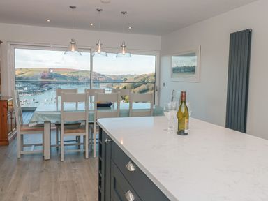 A dining area with a table and chairs by a large window overlooking a harbor at Moorings in Kingswear Devon