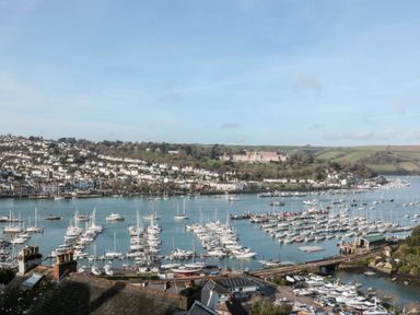A marina with numerous boats and yachts docked with a town and hills in the background at Moorings in Kingswear Devon
