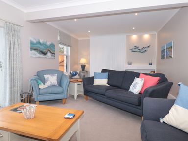A living room with blue and grey sofas and armchairs a wooden coffee table and coastal artwork at Moorings in Kingswear Devon